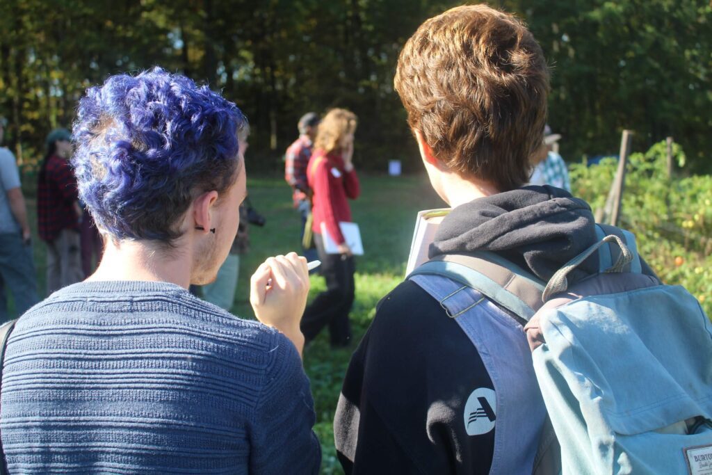 Two pre-apprentices with their backs turned away from the camera talking to each other while a group of apprentices walk in the background